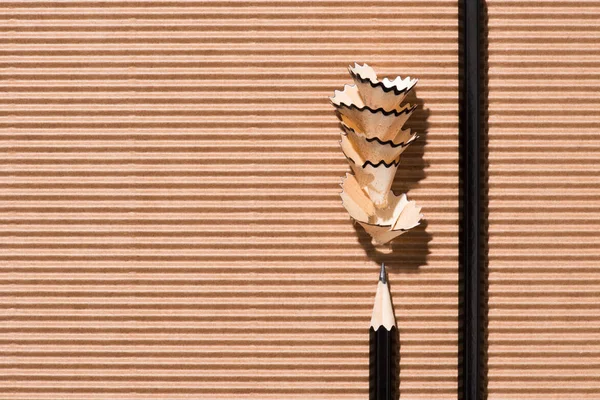 Top view of pencil shavings and black graphite pencils on cardboard — Stock Photo