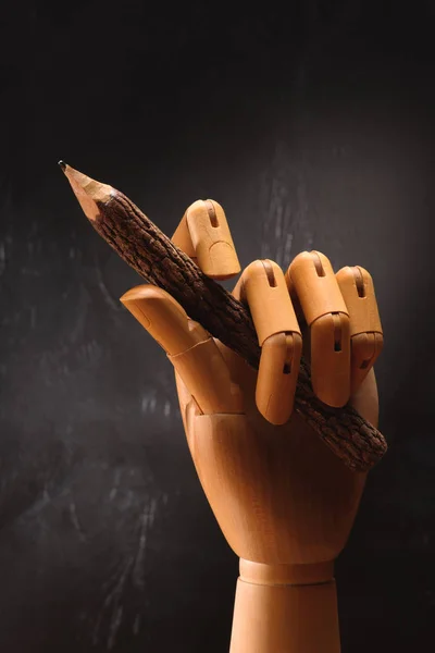 Close up of wooden hand holding pencil in front of empty chalkboard in school — Stock Photo