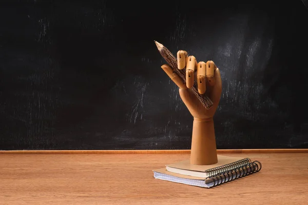 Close up view of textbooks under wooden hand holding pencil on desk in front of chalkboard in school — Stock Photo