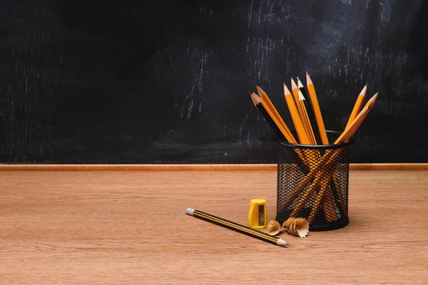 Close up view of desk organizer with pencils and sharpener on wooden table in front of empty chalk board in school — Stock Photo