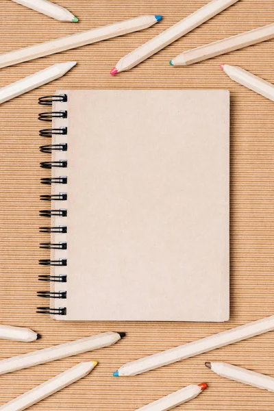 Flat lay com arranjo de caderno vazio e lápis coloridos no fundo marrom — Fotografia de Stock