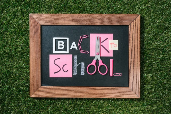 Vista superior de quadro-negro com letras de volta para a escola feitas de objetos rosa e branco no gramado verde — Fotografia de Stock