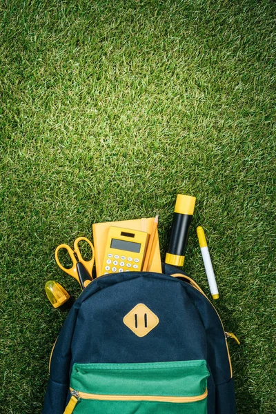 Flat lay com mochila arranjada e artigos de papelaria na grama verde — Fotografia de Stock