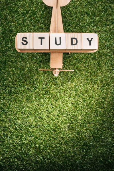 Top view of wooden toy plane and study inscription made of blocks on green grass — Stock Photo