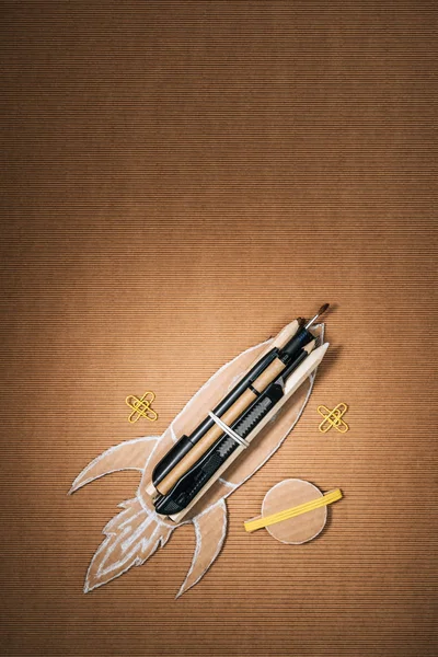 Vista superior del cohete de cartón hecho a mano con papelería y planeta sobre fondo marrón - foto de stock