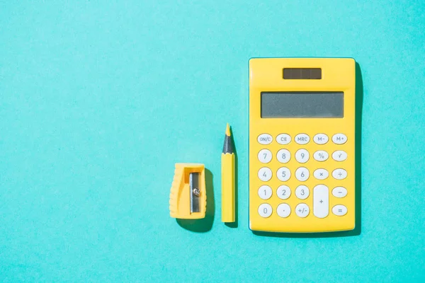 Vue du dessus de l'arrangement de la calculatrice, crayon et taille-crayon sur fond bleu — Photo de stock