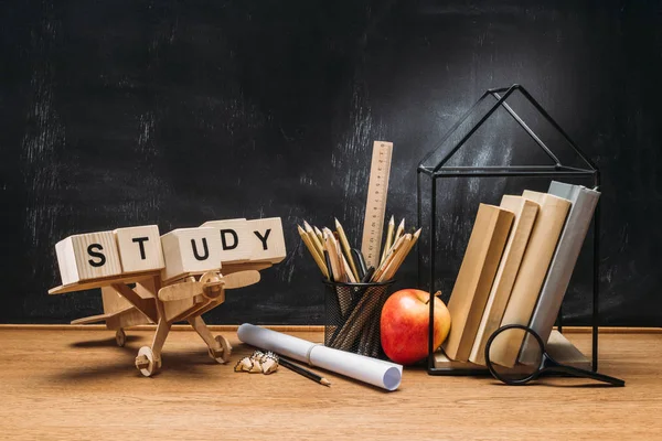 Nahaufnahme eines hölzernen Spielzeugflugzeugs, Studieninschrift aus Blöcken, Büchern und Bleistiften auf Tischplatte mit leerer Tafel dahinter — Stockfoto