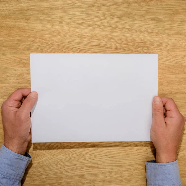 Cropped image of man holding empty white paper over wooden table — Stock Photo