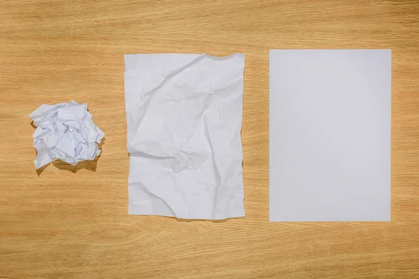 Vista superior de papeles arrugados y papel blanco en blanco sobre mesa de madera - foto de stock