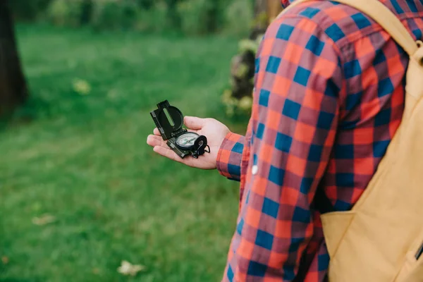 Cropped shot of young man in checkered shirt holding compass in forest — Stock Photo
