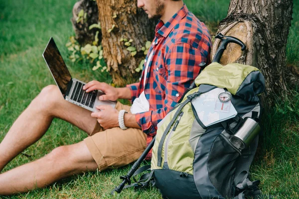 Plan recadré de jeune homme voyageur à l'aide d'un ordinateur portable avec écran vide tout en étant assis sur l'herbe — Photo de stock