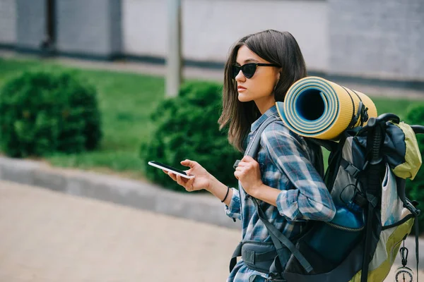 Молода жінка рюкзак в сонцезахисних окулярах тримає смартфон — стокове фото