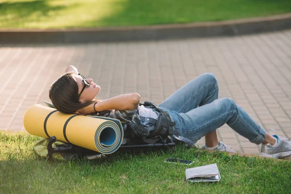 Mujer joven en gafas de sol acostada con mochila en la hierba — Stock Photo