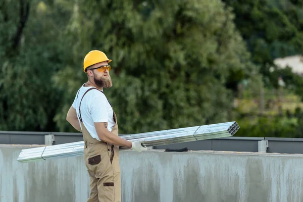 Bauarbeiter mit Schutzbrille und Schutzhelm trägt Metallkonstruktionen auf Baustelle — Stockfoto