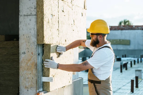 Constructor en casco protector y googles haciendo aislamiento de la pared en el sitio de construcción - foto de stock