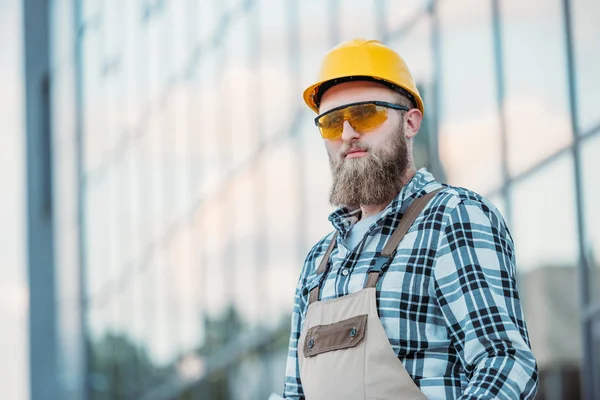 Enfoque selectivo del trabajador de la construcción en googles protectores y hardhat mirando hacia otro lado - foto de stock