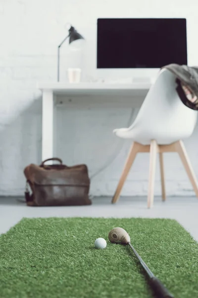 Golf club and ball on green grass carpet in light modern office — Stock Photo