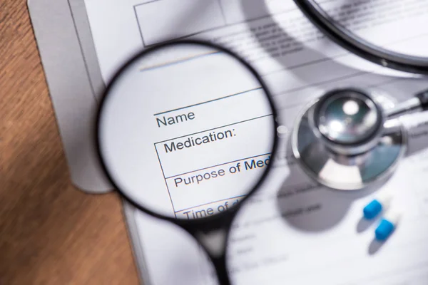 Blick von der Lupe auf den medizinischen Fragebogen auf dem Tisch mit Stethoskop und Pillen — Stockfoto