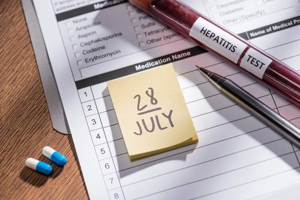 Selective focus of stick it 28th july date, medical questionary, pills and test flask with lettering hepatitis test on table — Stock Photo