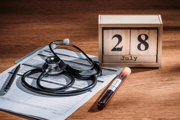 Selective focus of test flask with blood sample, stethoscope, medical questionary and wooden calendar with 28th july date on table, world hepatitis day concept — Stock Photo