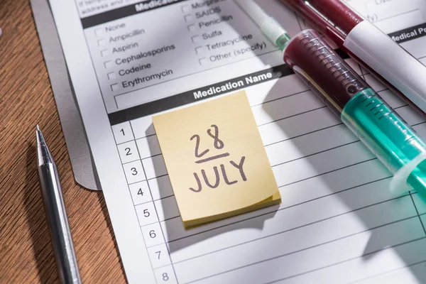 Selective focus of stick it 28th july date, medical questionnaire, syringe and test flask with blood samples, world hepatitis day concept — Stock Photo