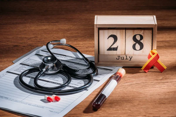 Foco seletivo do calendário de madeira com data de 28 de julho, questionário médico, pílulas, estetoscópio, frasco de teste com amostra de sangue, conceito mundial do dia da hepatite — Fotografia de Stock