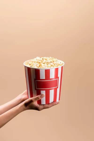 Partial view of woman holding disposable bucket with popcorn isolated on beige — Stock Photo