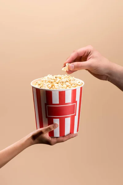 Cropped shot of male and female hands with disposable bucket with popcorn isolated on beige — Stock Photo