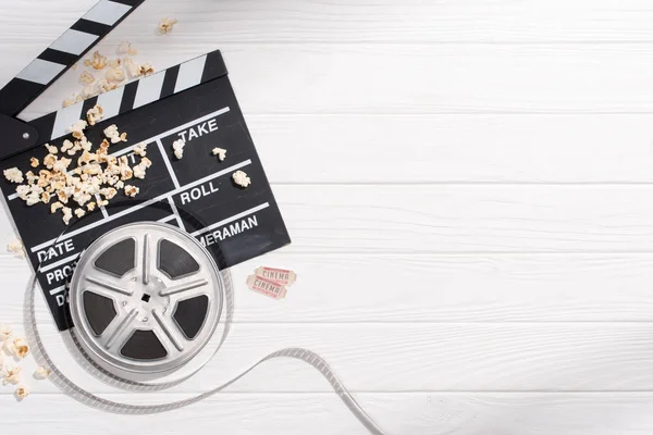 Плоский уголок с доской для хлопка, фильмлентами, попкорном и билетами в ретро-кино на белой деревянной столешнице — стоковое фото