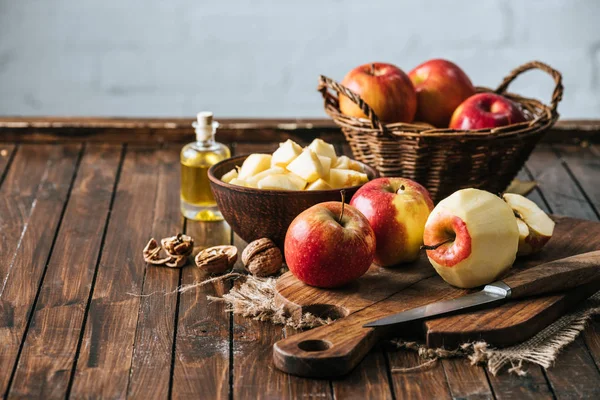 Close up view of bottle of juice, fresh apples on cutting board, hazelnuts and knife on wooden surface — Stock Photo