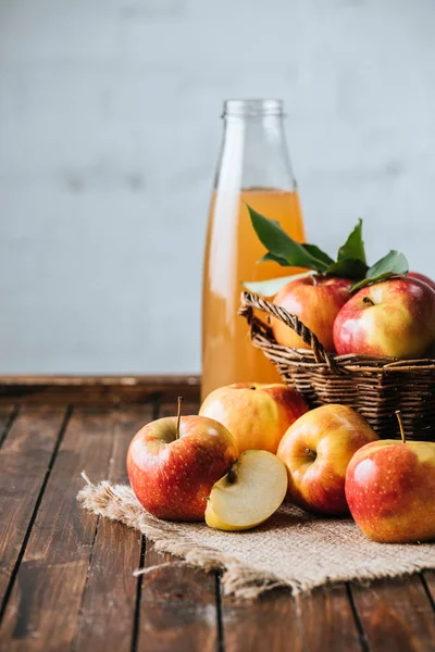 Vista de perto de garrafa de vidro de suco de maçã e maçãs em cesta na mesa de madeira — Fotografia de Stock