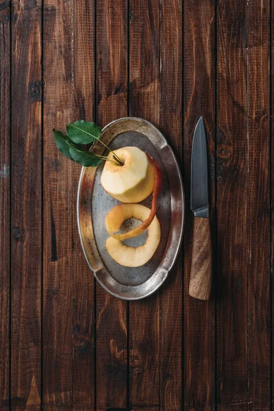 Top view of peeled apple on metal tray and knife on wooden tabletop — Stock Photo