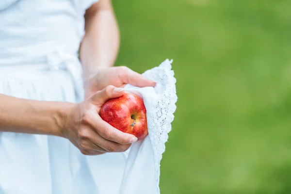 Vista recortada de niña limpiando manzana roja con delantal - foto de stock
