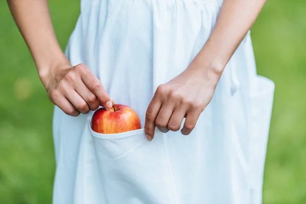 Cropped view of girl putting apple into pocket — Stock Photo