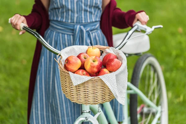 Vista recortada de chica con cesta de mimbre llena de manzanas en bicicleta - foto de stock