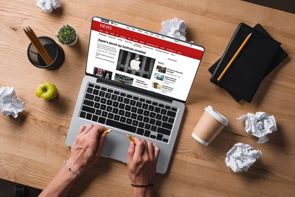 Abgeschnittene Aufnahme eines Geschäftsmannes, der am Arbeitsplatz einen Bleistift zerbricht, während er sich die bbc-Website auf dem Bildschirm des Laptops ansieht — Stockfoto