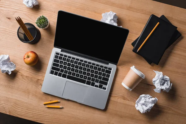 Vue du dessus du lieu de travail désordonné avec ordinateur portable, café à emporter et papiers froissés — Photo de stock