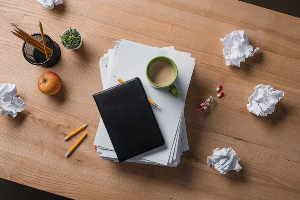 Draufsicht auf gestapelte Blankopapiere mit Tasse Kaffee und Notizbuch auf Holztisch — Stockfoto
