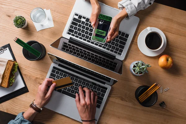 Schnappschuss von Geschäftsmann beim E-Shopping, während sein Kollege Smartphone mit Buchungs-App am Arbeitsplatz nutzt — Stockfoto