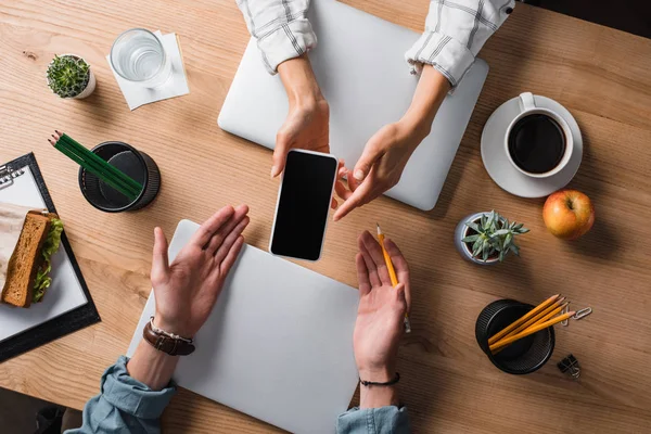 Cropped shot of businesswoman showing smartphone with blank screen to colleague at workplace — Stock Photo