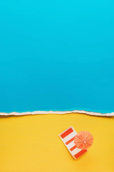 Top view of little cocktail umbrella and bedding on yellow and blue paper backdrop — Stock Photo