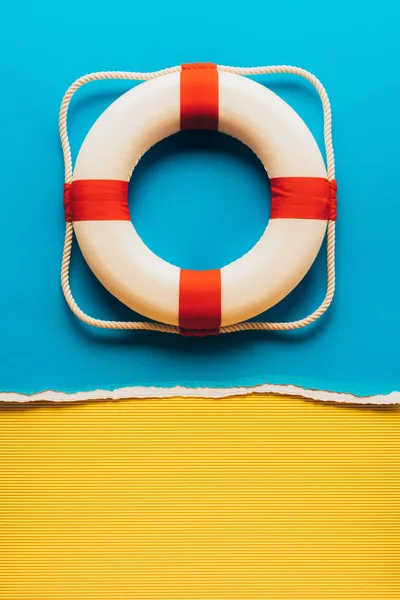 Vue du dessus du sauveteur de vie rouge et blanc sur fond papier bleu et jaune — Photo de stock
