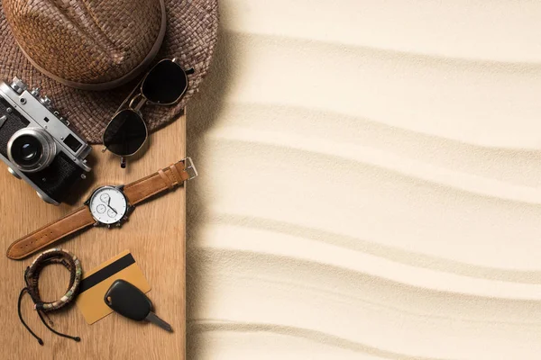 Pose plate avec accessoires masculins pour voyager sur une planche de bois sur une plage de sable — Photo de stock