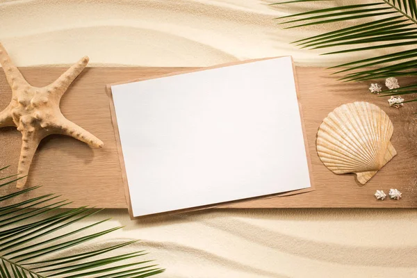 Flat lay with palm leaves, blank paper, sea star and seashells on wooden plank on sand — Stock Photo