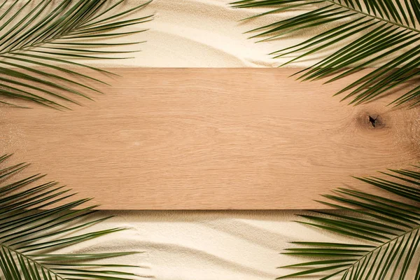 Vue de dessus des feuilles de palmier et de la planche de bois sur une surface sablonneuse — Photo de stock