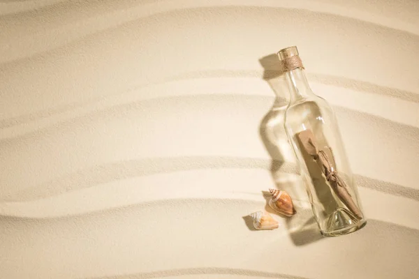 Flat lay with paper roll in glass bottle and seashells on sand — Stock Photo