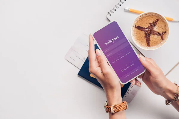 Schnappschuss einer Frau mit Smartphone mit Instagram-Logo auf dem Bildschirm am Tisch mit Tasse Kaffee, Ticket und Reisepass — Stockfoto