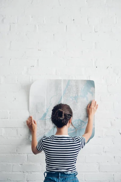 Visão traseira da mulher olhando mapa em mãos na parede de tijolo branco, conceito de viagem — Fotografia de Stock