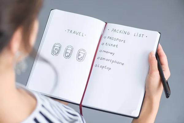 Partial view of woman with pen holding notebook with packing list for traveling — Stock Photo