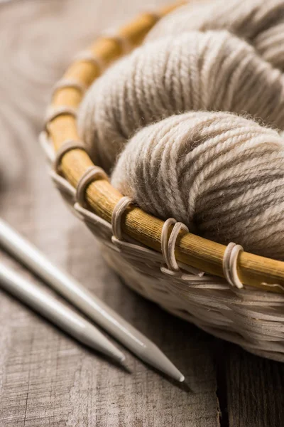 Messa a fuoco selettiva di filato di lana lavorato a maglia beige in cesto di vimini vicino ad aghi lavorati a maglia su sfondo di legno — Foto stock